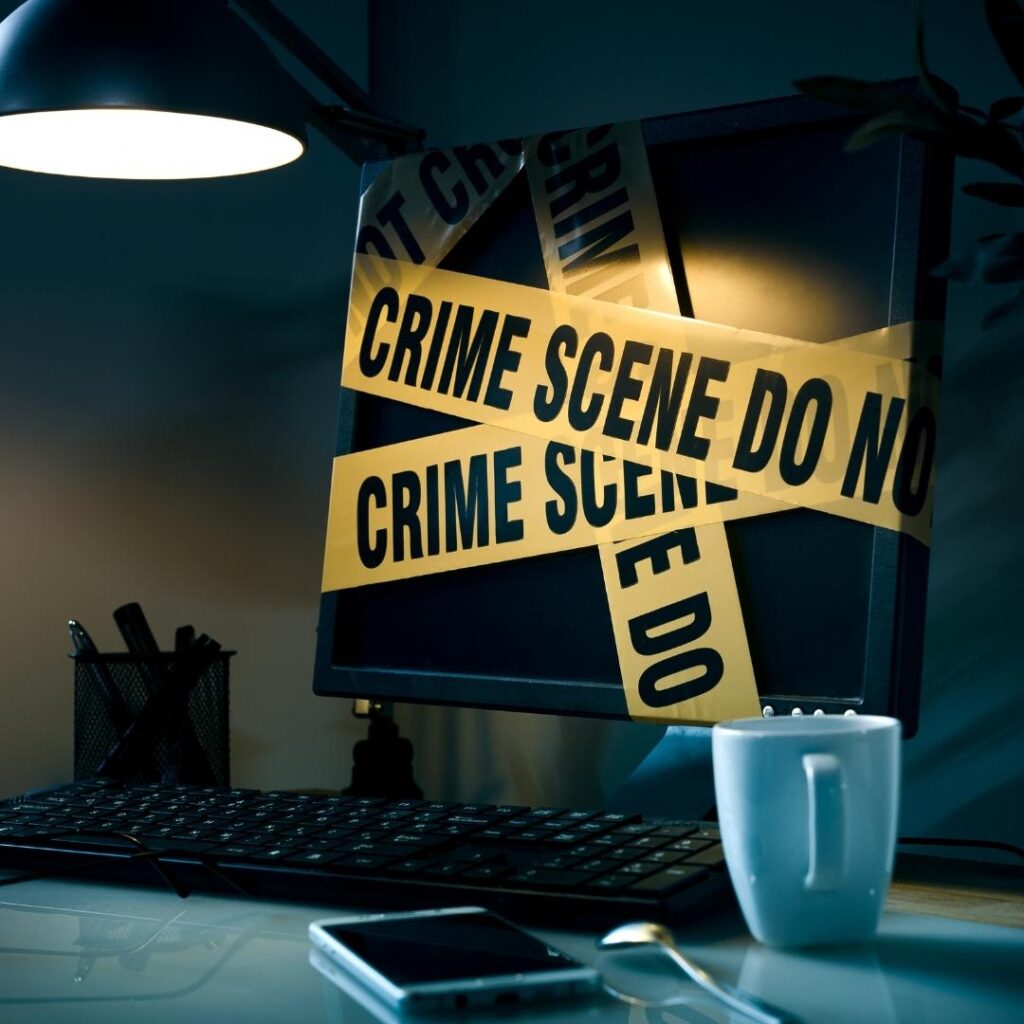 Computer wrapped in crime scene tape next to a phone and coffee mug