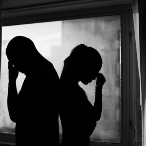 Silhouette of a couple with their backs to each other. They are stressed.